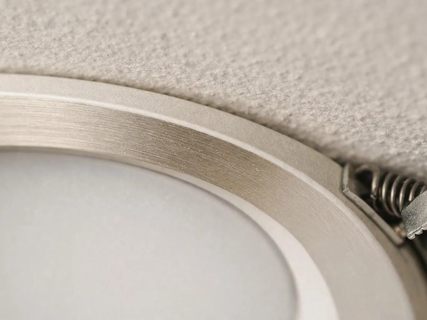 Close-up of a round recessed light fixture with a spring clip against a textured ceiling