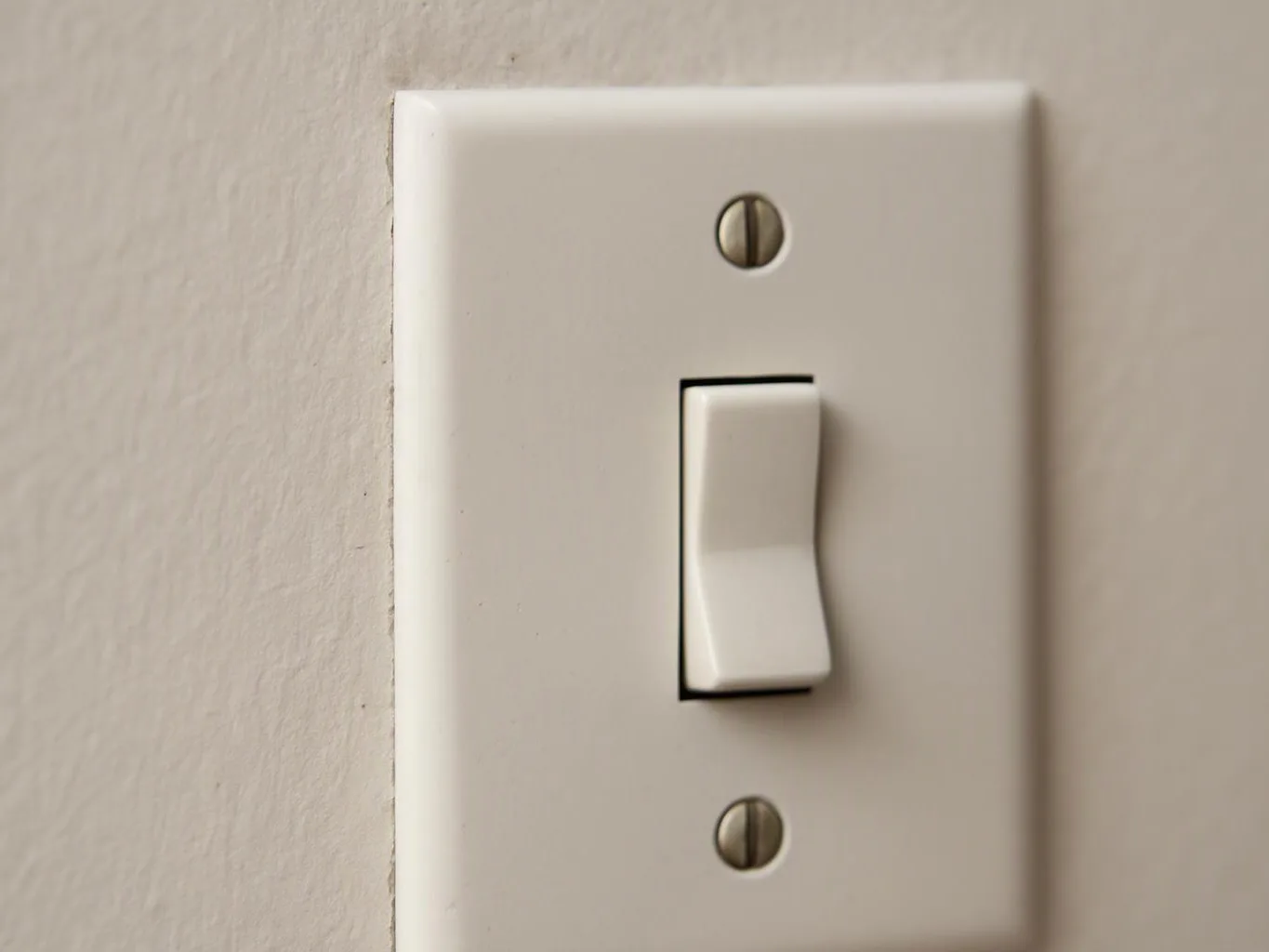A white wall light switch plate sits on a beige wall in close-up